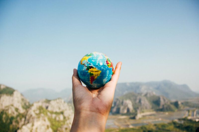 Hand hält einen kleinen Globus vor einer Landschaft